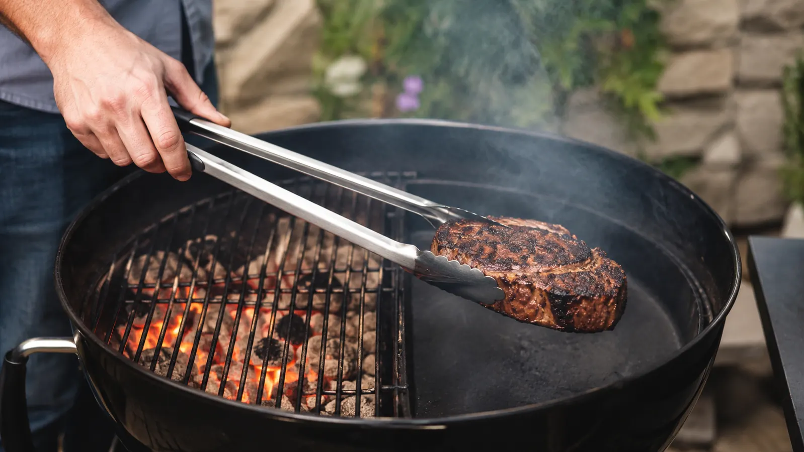 Thick bone-in chicken thighs cooking on the indirect side of a charcoal grill with the lid on and a small orange glow visible through the vents